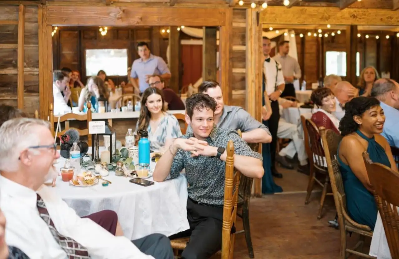 Guests seated at round tables with white tablecloths in the barn's wood-paneled dining room.