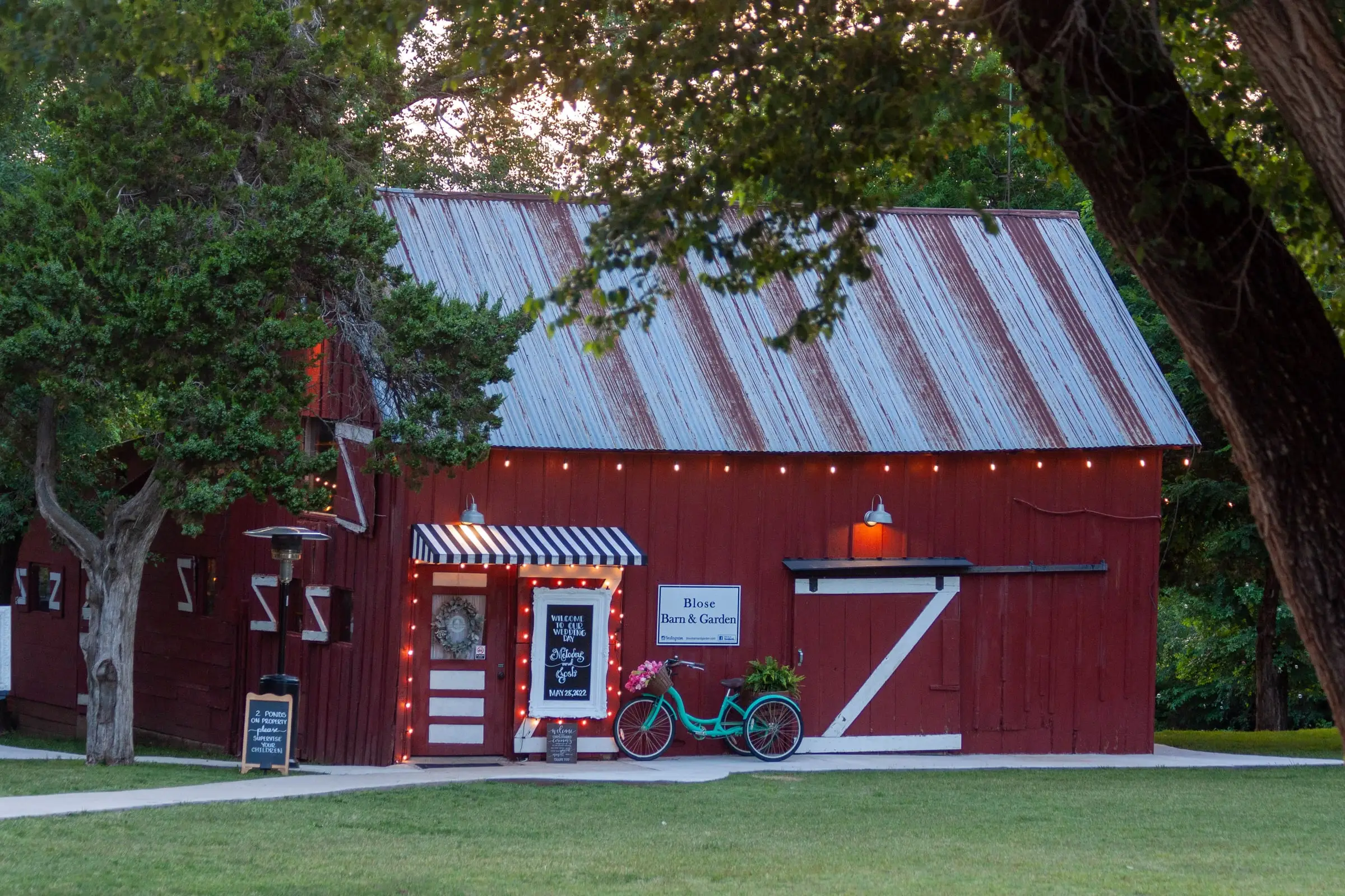 The red barn under tall shade trees, its doors and windows trimmed in white.