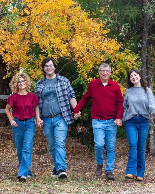 Four members of the Blose family walking hand in hand among the trees in fall.