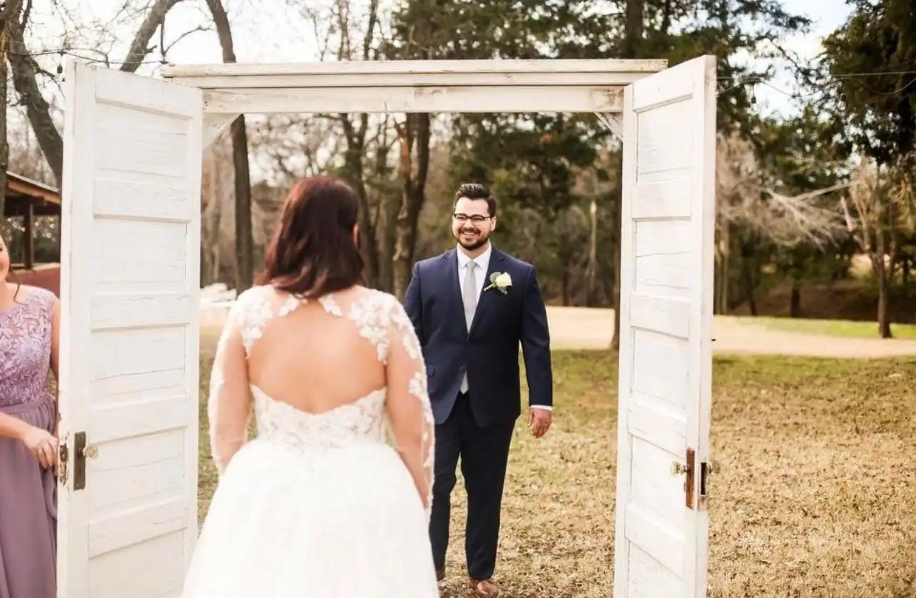 A bride steps through white double doors toward her groom for their first look.