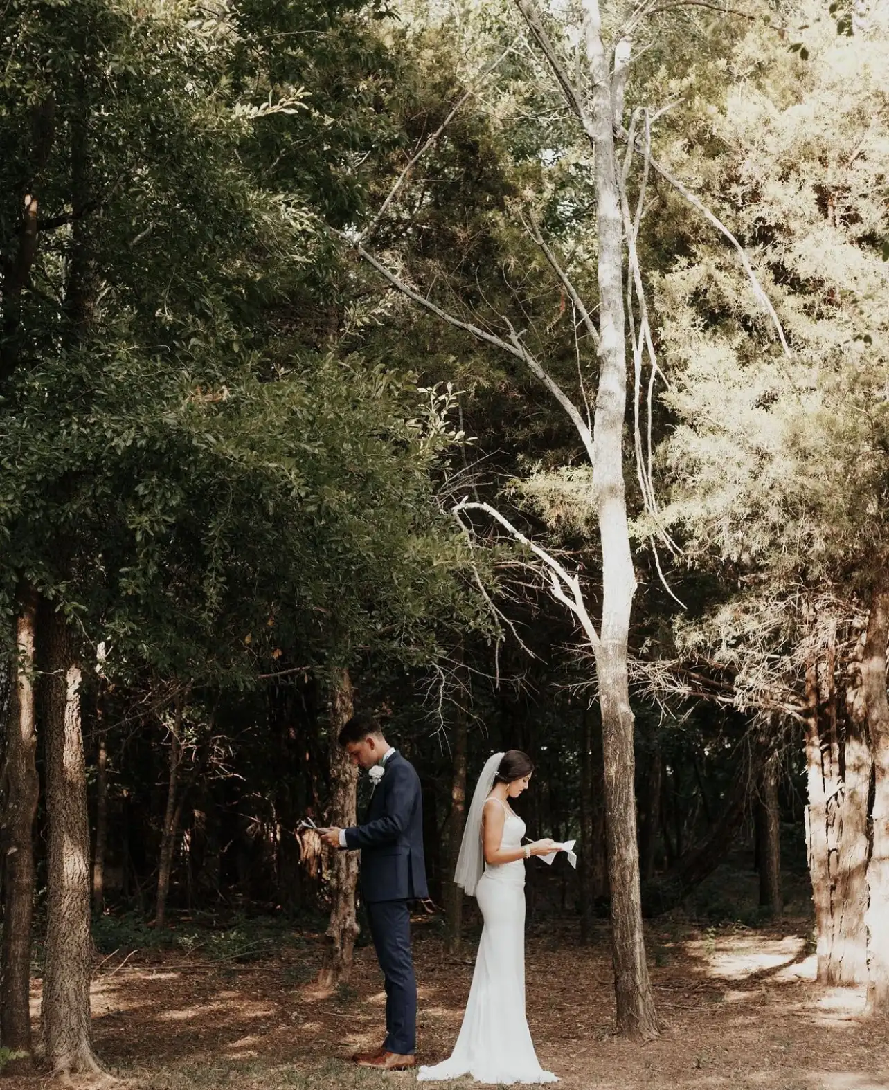 A bride and groom face each other for a first look in the woods.