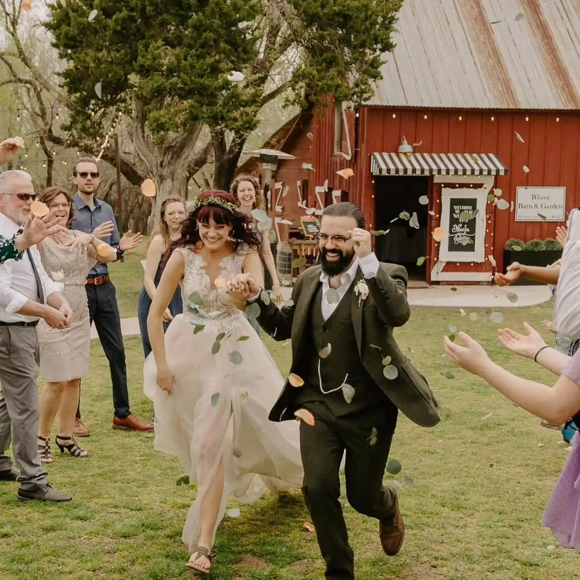 Guests toss petals as a bride and groom run past the red barn.
